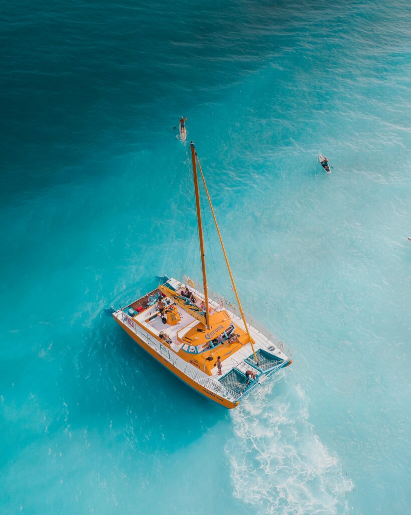 Aerial view of a colorful catamaran sailing on turquoise waters with people enjoying a sunny day.